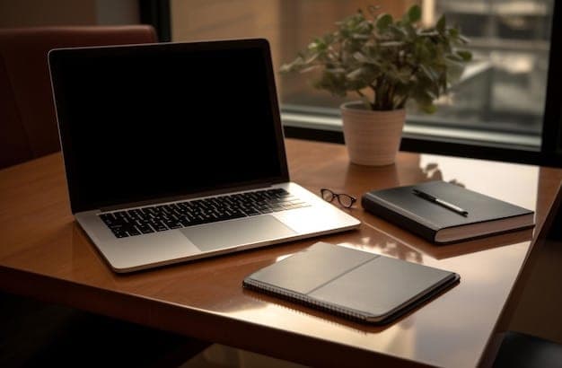 An open laptop with a blank dark screen on a wooden desk, beside a closed notebook, a pen and a small potted plant